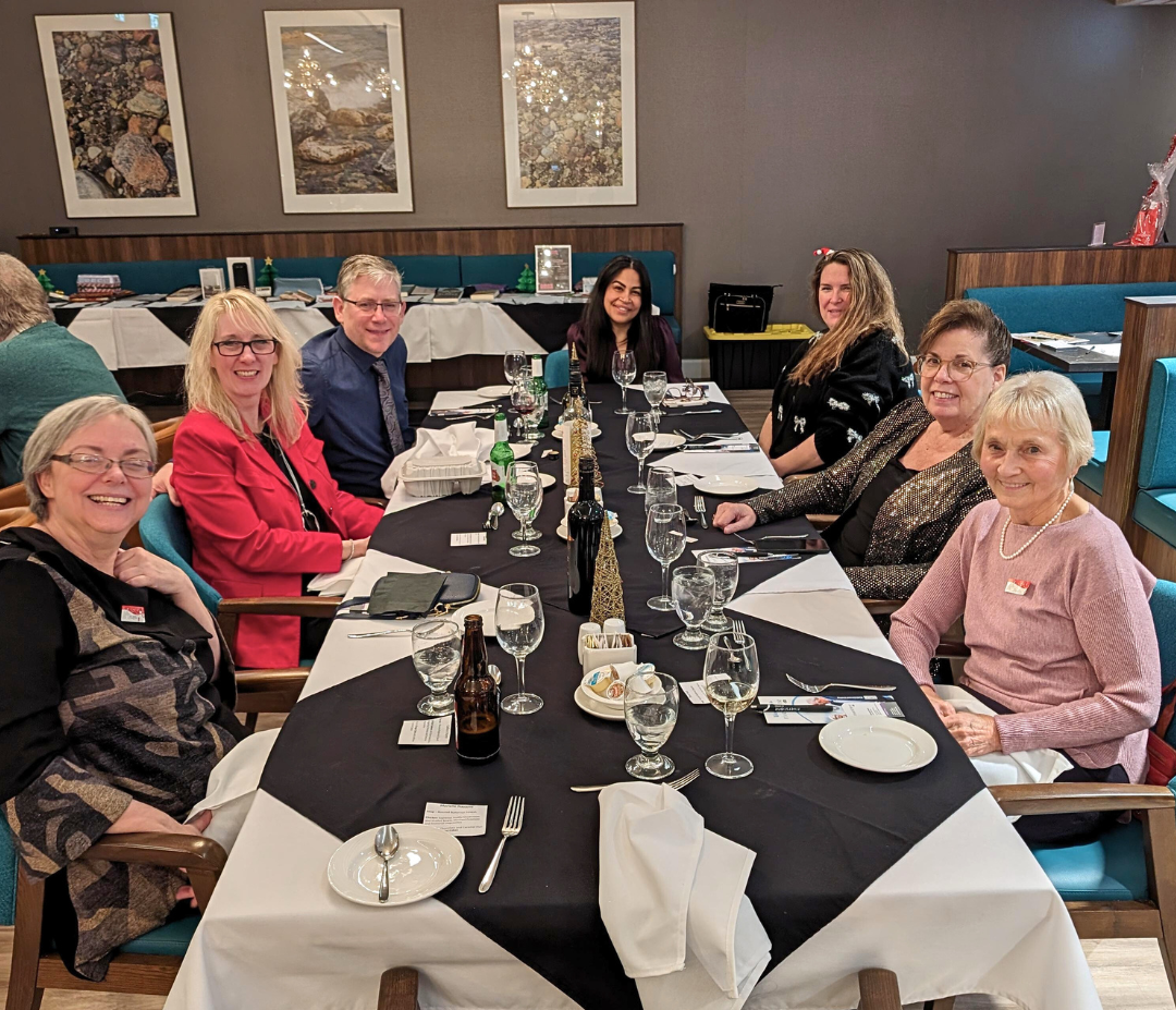 Tammie Ross is the woman in red blazer sitting in between a man with glasses and blue shirt and another woman with glasses in black with gold design blouse. With them are four other women who are having a meal.